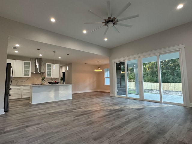 kitchen with wall chimney range hood, hardwood / wood-style flooring, decorative light fixtures, white cabinetry, and stainless steel refrigerator