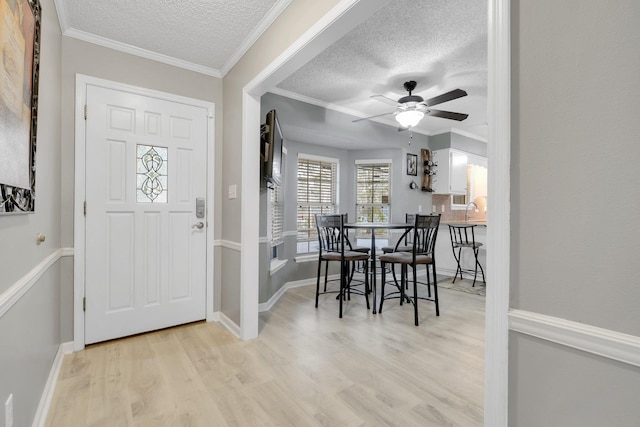 foyer featuring a textured ceiling, ornamental molding, ceiling fan, and light wood-type flooring