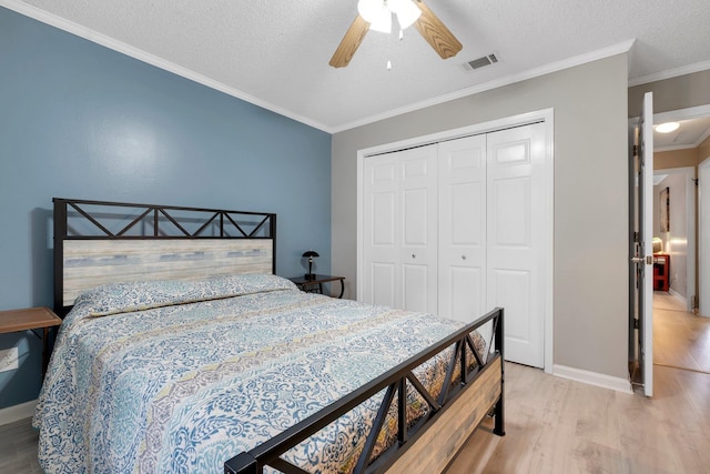 bedroom with a textured ceiling, ornamental molding, a closet, ceiling fan, and light hardwood / wood-style floors