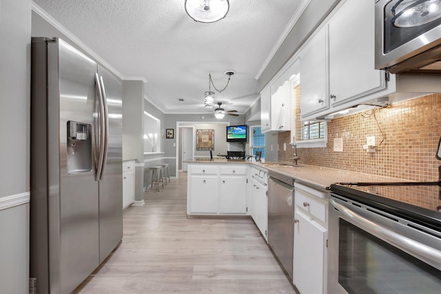 kitchen with white cabinetry, ornamental molding, kitchen peninsula, stainless steel appliances, and light wood-type flooring