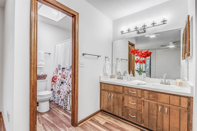 bathroom with hardwood / wood-style flooring, ceiling fan, a skylight, vanity, and toilet