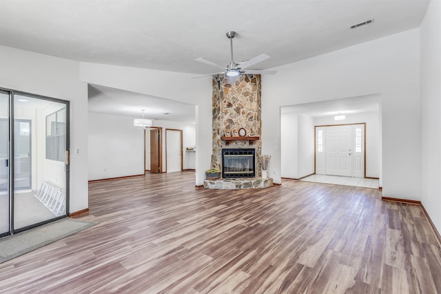 unfurnished living room featuring ceiling fan, a stone fireplace, vaulted ceiling, and light hardwood / wood-style flooring