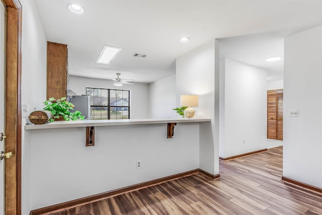 kitchen with hardwood / wood-style flooring, a breakfast bar area, stainless steel refrigerator, ceiling fan, and kitchen peninsula