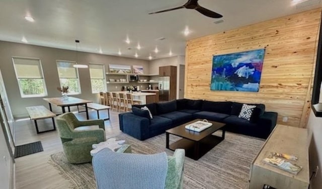 living room with wood walls, ceiling fan, and light wood-type flooring