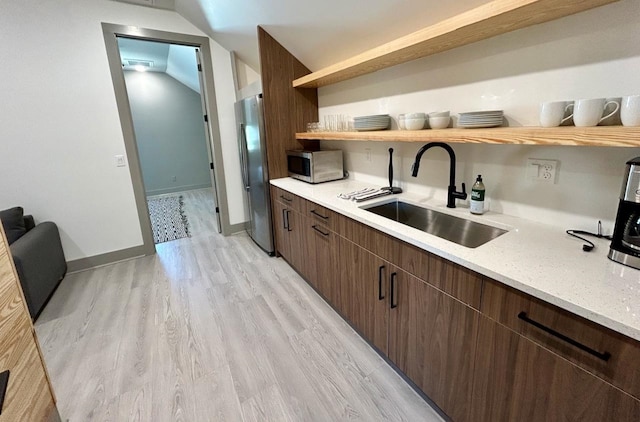 kitchen featuring lofted ceiling, sink, appliances with stainless steel finishes, light hardwood / wood-style floors, and dark brown cabinetry