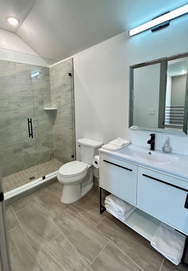 bathroom featuring vanity, toilet, a shower with door, and vaulted ceiling