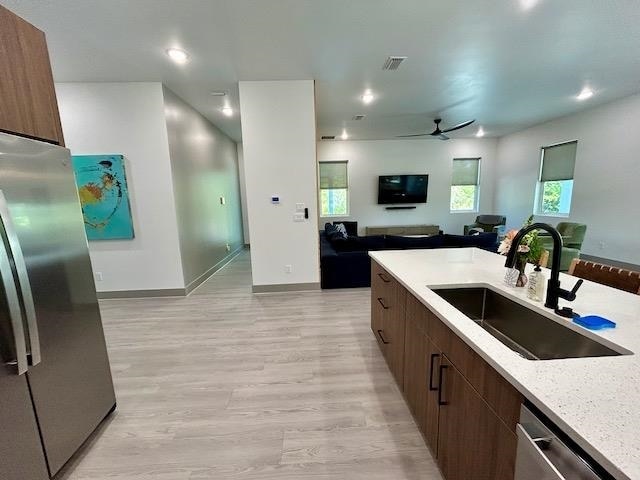 kitchen featuring light stone countertops, ceiling fan, sink, stainless steel appliances, and light wood-type flooring