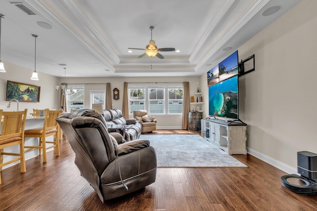 living room with wood-type flooring, a raised ceiling, ceiling fan, and ornamental molding