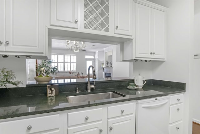 kitchen with dark stone counters, white dishwasher, a notable chandelier, white cabinets, and a sink