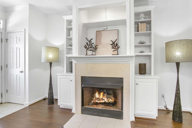 living room with a tiled fireplace, crown molding, built in shelves, and wood finished floors