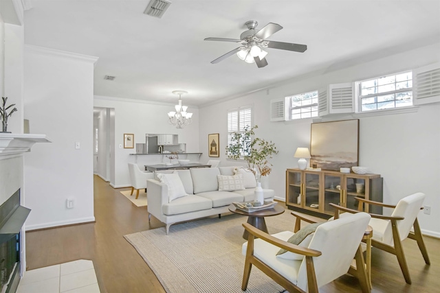 living area featuring visible vents, crown molding, ceiling fan with notable chandelier, a fireplace, and wood finished floors