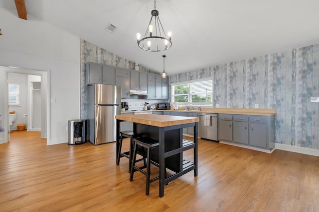 kitchen with light wood-type flooring, appliances with stainless steel finishes, hanging light fixtures, and butcher block countertops