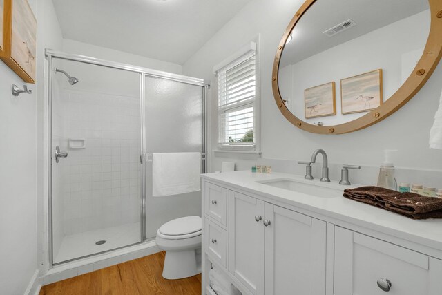 bathroom featuring wood-type flooring, toilet, vanity, and a shower with shower door