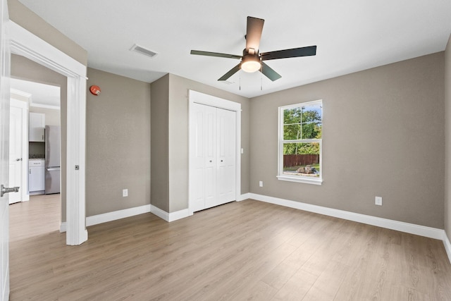 unfurnished bedroom featuring light hardwood / wood-style flooring, ceiling fan, stainless steel refrigerator, and a closet