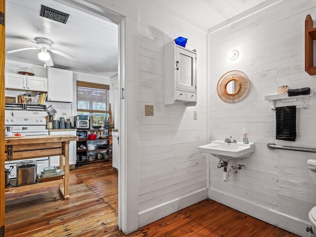 bathroom featuring wood-type flooring, wooden walls, sink, toilet, and ceiling fan