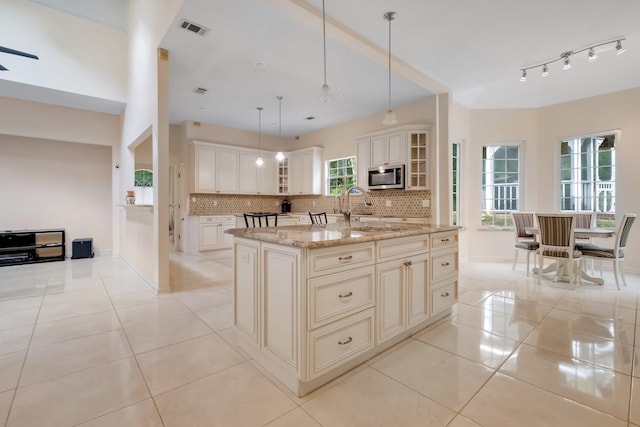 kitchen with decorative backsplash, a kitchen island with sink, hanging light fixtures, light stone countertops, and sink