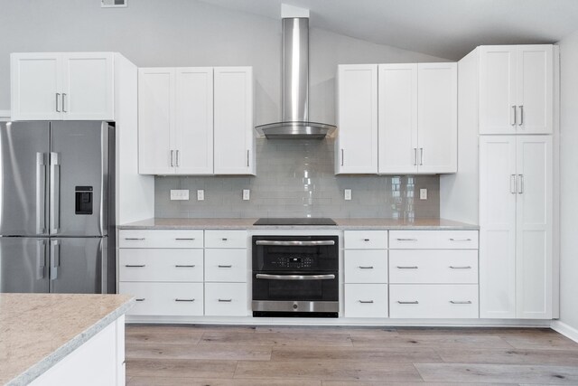 82 Royster Dr, Crawfordville, FL 32327 - kitchen featuring stainless steel appliances, wall chimney range hood, vaulted ceiling, white cabinetry, and tasteful backsplash