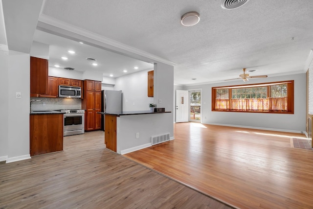 kitchen with appliances with stainless steel finishes, backsplash, ornamental molding, kitchen peninsula, and light wood-type flooring