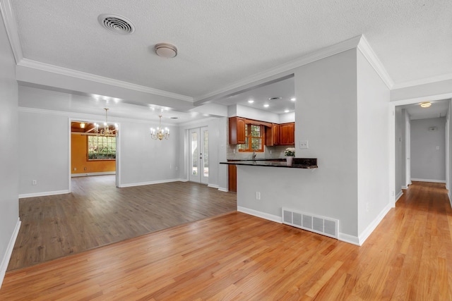 unfurnished living room with a textured ceiling, a chandelier, and light hardwood / wood-style flooring