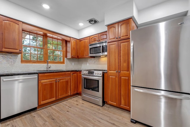 kitchen featuring appliances with stainless steel finishes, light hardwood / wood-style floors, sink, and backsplash