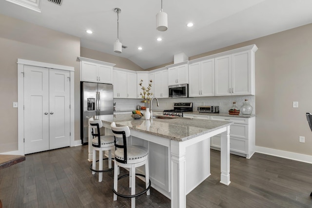 kitchen featuring appliances with stainless steel finishes, decorative light fixtures, white cabinetry, an island with sink, and backsplash