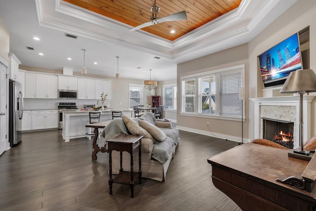 living room with a stone fireplace, wooden ceiling, a raised ceiling, dark wood-type flooring, and crown molding