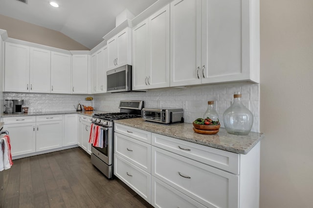 kitchen featuring white cabinetry, appliances with stainless steel finishes, tasteful backsplash, light stone countertops, and vaulted ceiling