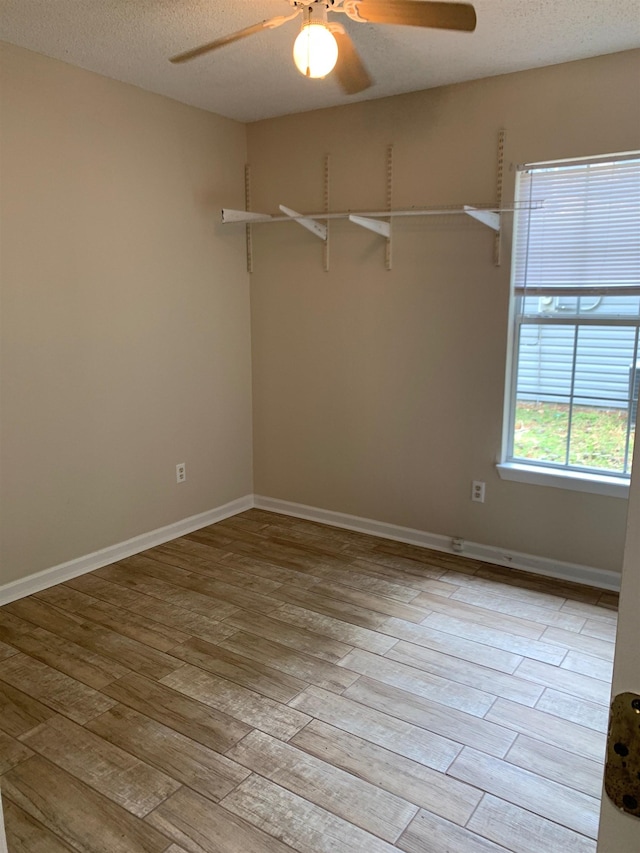 empty room with light wood-type flooring, baseboards, and a textured ceiling