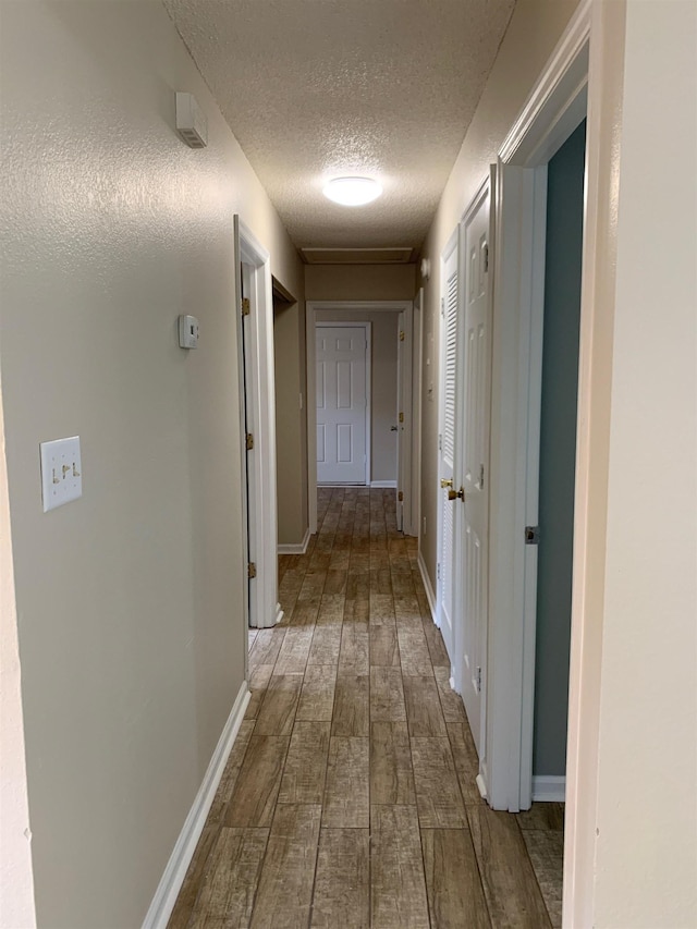 hallway featuring wood tiled floor, baseboards, and a textured ceiling