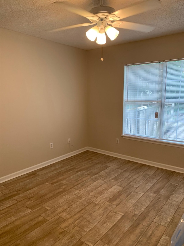 empty room featuring a textured ceiling, ceiling fan, wood finished floors, and baseboards