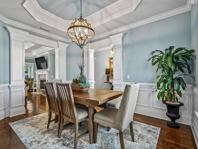 dining area featuring ornate columns, dark hardwood / wood-style flooring, ornamental molding, a raised ceiling, and an inviting chandelier