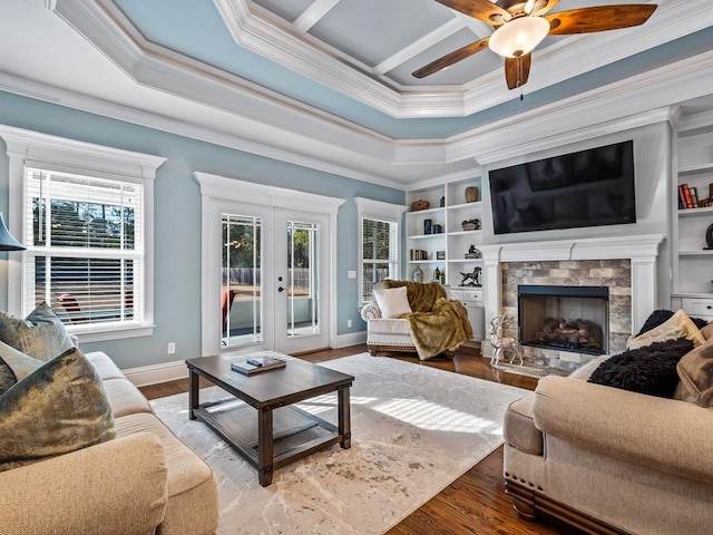 living room with ornamental molding, a stone fireplace, hardwood / wood-style floors, and french doors