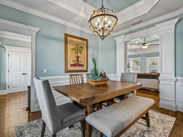 dining space featuring ornate columns, ornamental molding, dark wood-type flooring, and ceiling fan with notable chandelier