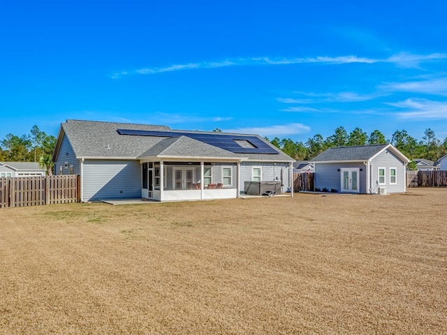 rear view of house featuring an outbuilding, a yard, a sunroom, and solar panels