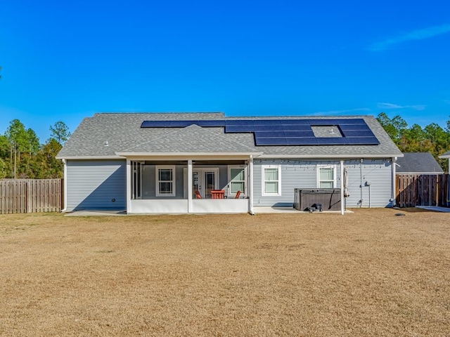 back of house featuring a patio area, a hot tub, solar panels, and a lawn