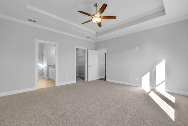 unfurnished bedroom featuring crown molding, a spacious closet, light carpet, and a tray ceiling