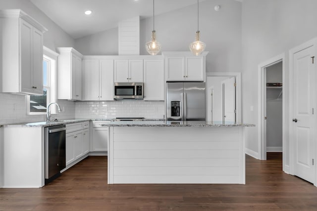 kitchen with stainless steel appliances, a kitchen island, white cabinets, and light stone counters