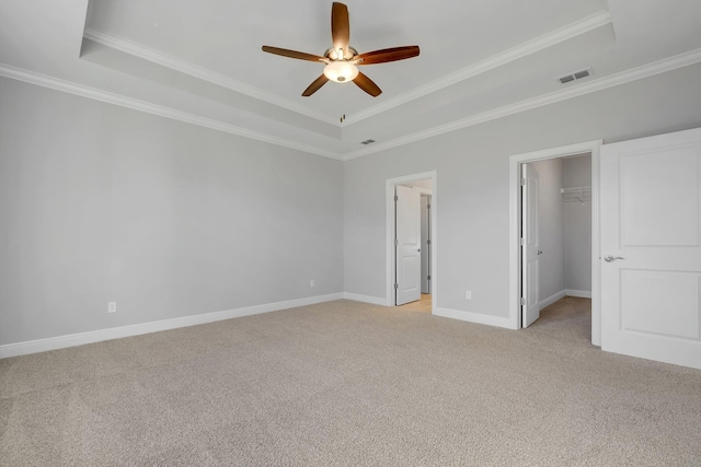 unfurnished bedroom with ceiling fan, a walk in closet, ornamental molding, and a tray ceiling