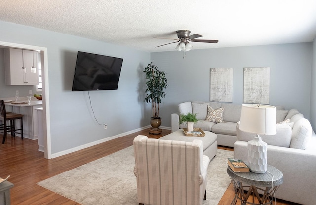 living room featuring ceiling fan, a textured ceiling, baseboards, and wood finished floors