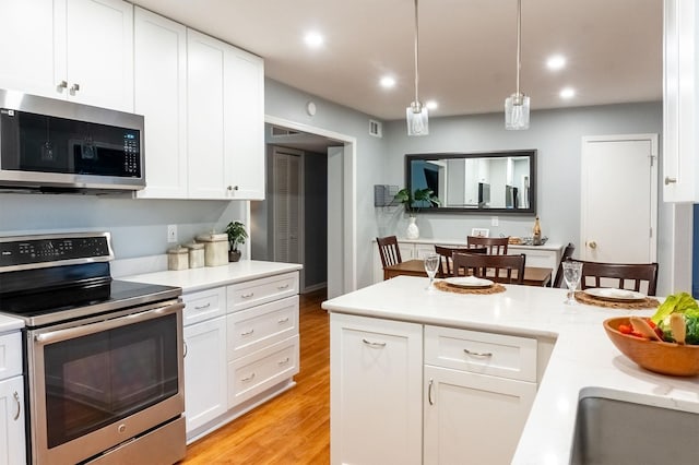 kitchen with white cabinets, light wood-style flooring, appliances with stainless steel finishes, light countertops, and pendant lighting