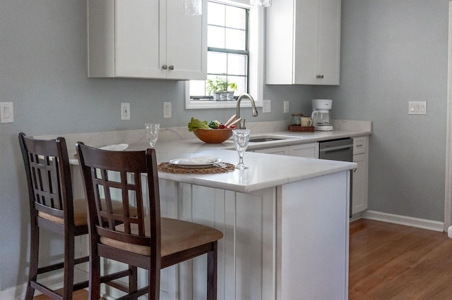 kitchen featuring a peninsula, a sink, white cabinetry, a kitchen breakfast bar, and light countertops