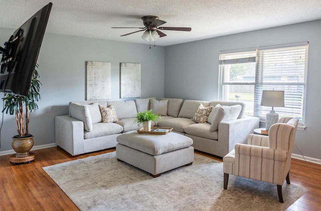 living area featuring ceiling fan, a textured ceiling, baseboards, and wood finished floors