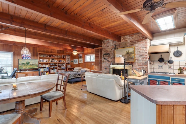 living room with beam ceiling, ceiling fan, light hardwood / wood-style flooring, wood walls, and a fireplace