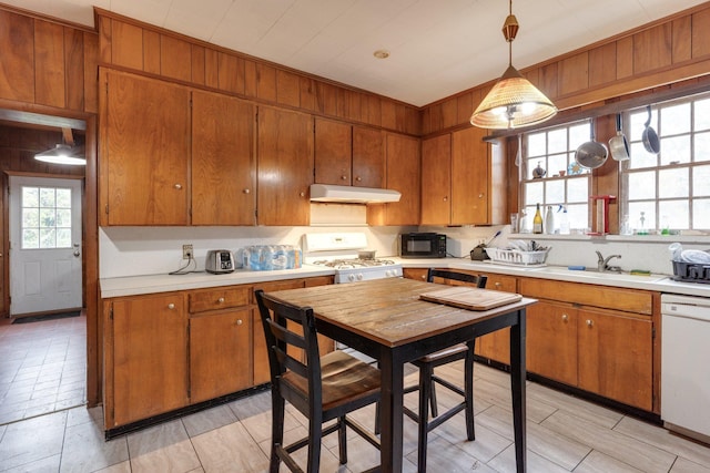 kitchen featuring decorative light fixtures, white appliances, sink, and wooden walls