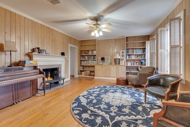 sitting room featuring ornamental molding, built in shelves, ceiling fan, wooden walls, and light hardwood / wood-style flooring