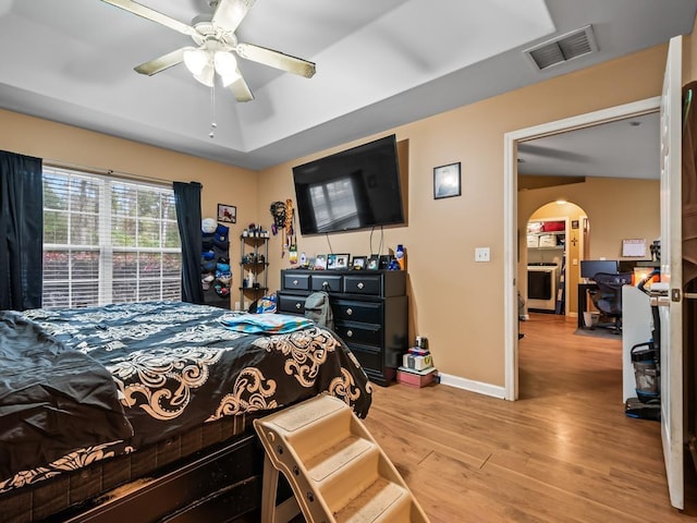 bedroom with ceiling fan, light hardwood / wood-style floors, and a raised ceiling