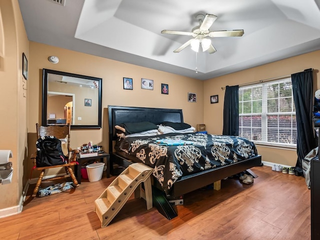 bedroom with hardwood / wood-style flooring, a raised ceiling, and ceiling fan