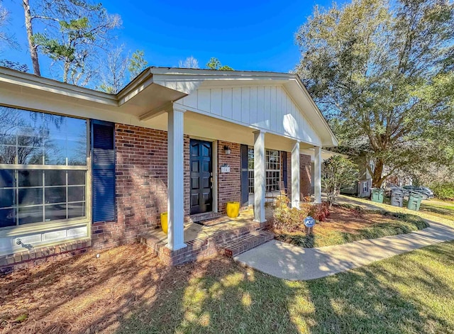 doorway to property featuring covered porch and brick siding