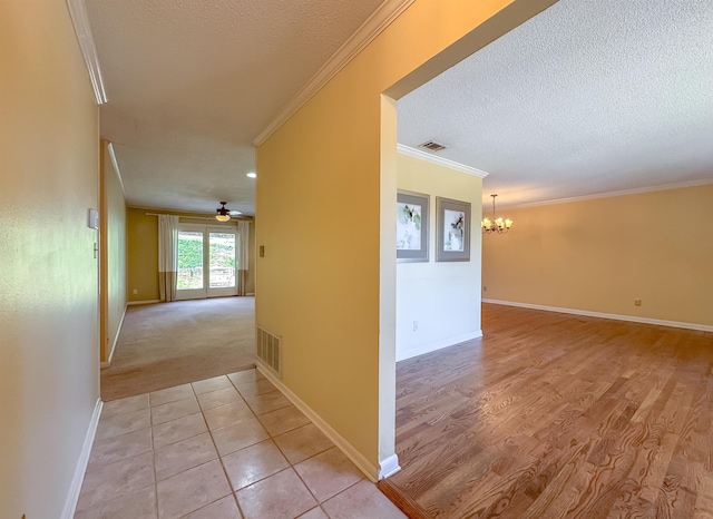 corridor featuring a chandelier, a textured ceiling, visible vents, and crown molding