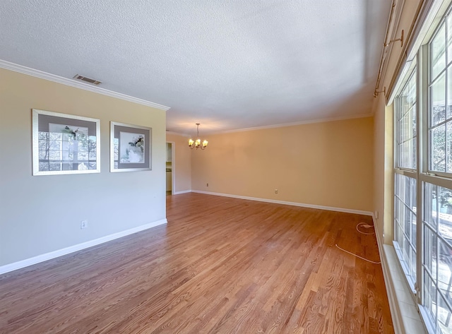 spare room with light wood-type flooring, an inviting chandelier, a textured ceiling, and crown molding